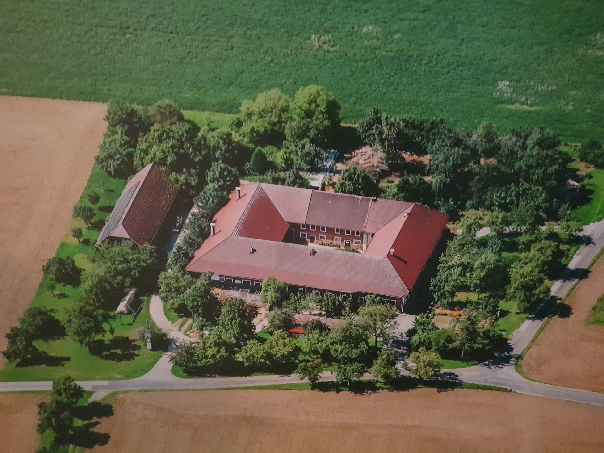 Luftaufnahme eines großen, rechteckigen Gebäudekomplexes mit Innenhof, umgeben von Bäumen und Feldern.